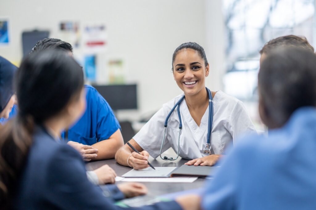 A female nurse smiling at a table with colleagues.