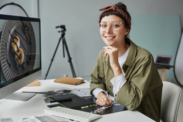 A woman sitting at a desk, using a computer and a camera for work.